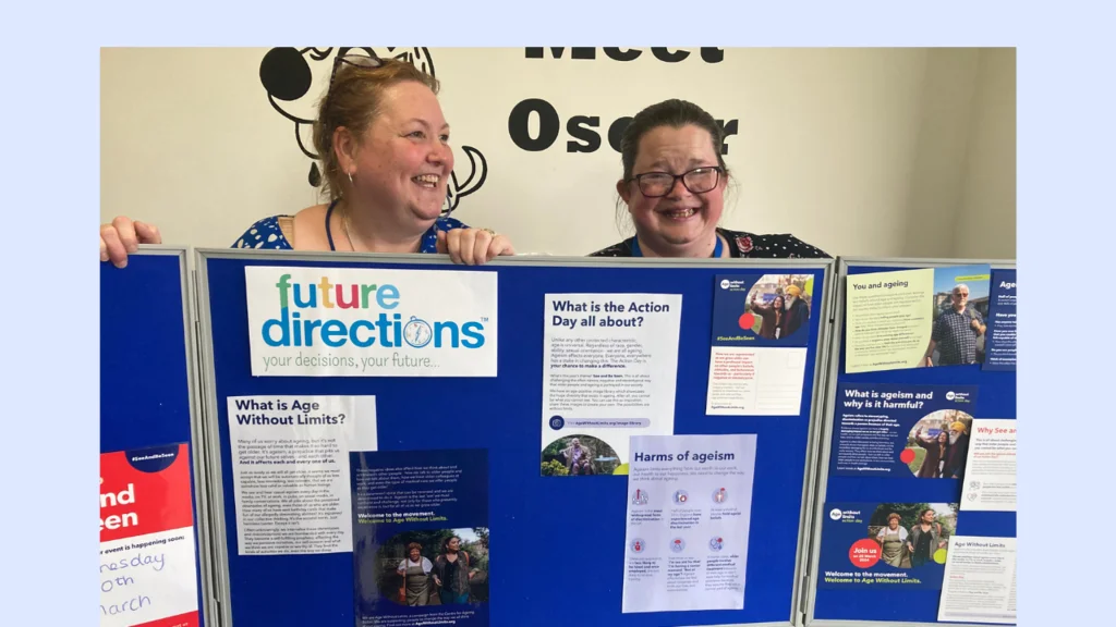 Two women hold up a display board which features the Future Directions logo and Age Without Limits Action Day materials.